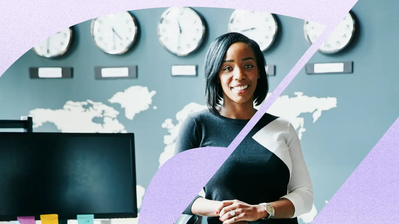 A person stands in front of a world map wall with multiple clocks, near a desk with sticky notes.
