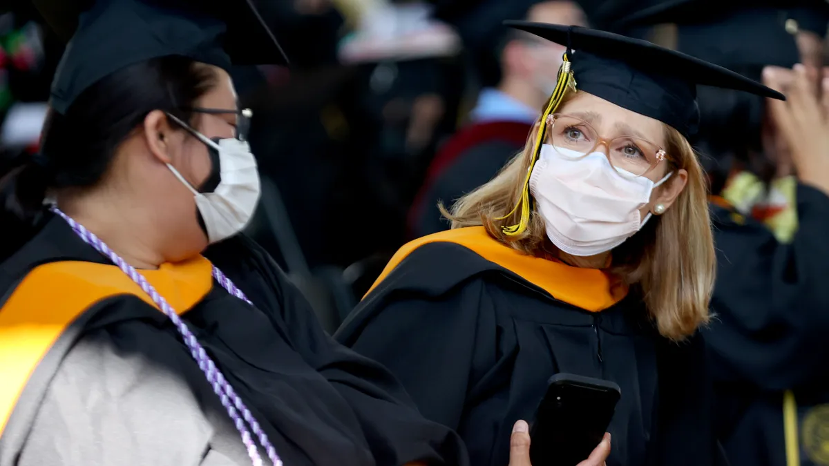 Two people dressed in graduation caps and gowns wear masks at their commencement.