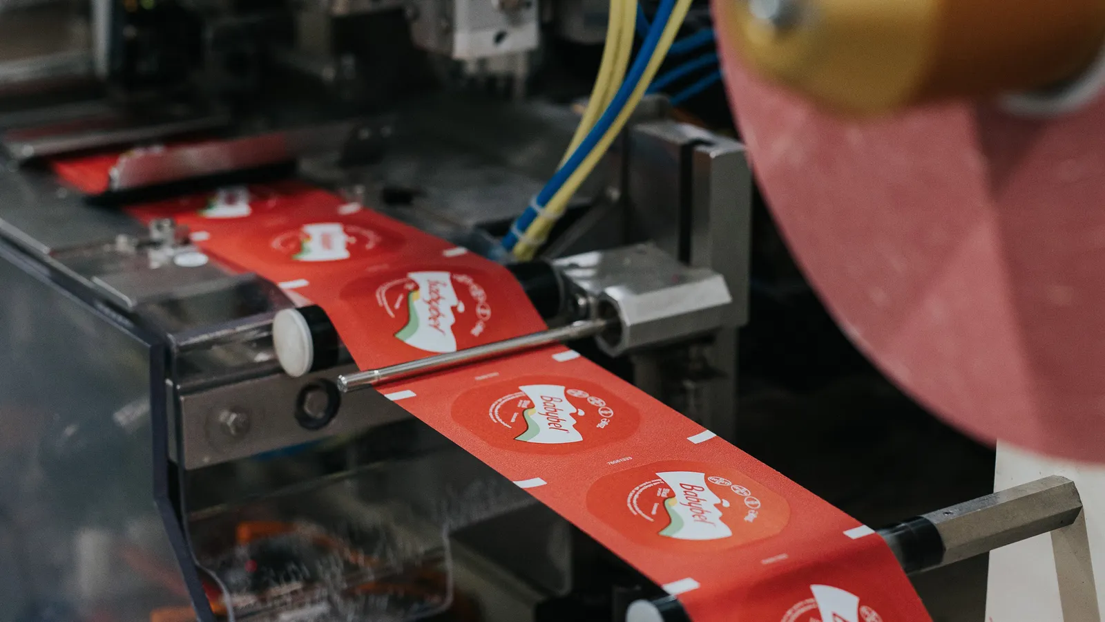 Red wrappers for Babybel cheese weave through industrial equipment.