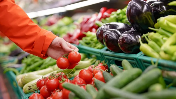 Closeup of a person picking up tomatoes at a grocery store.