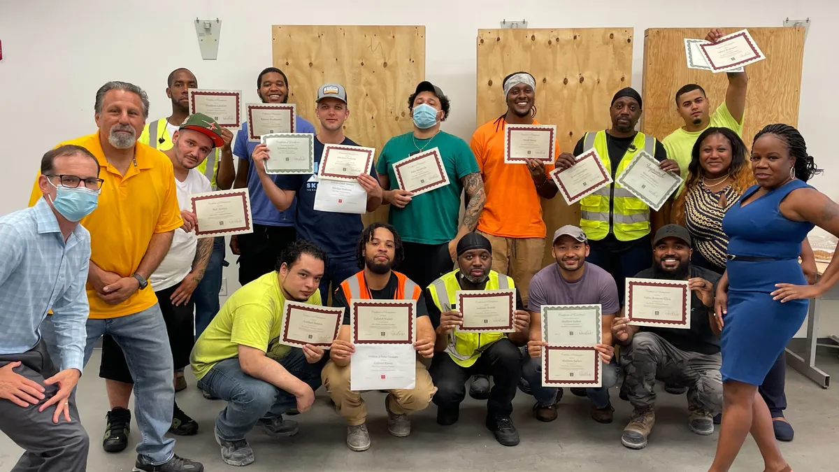 Several people in construction gear and civilian clothes pose with certificates.