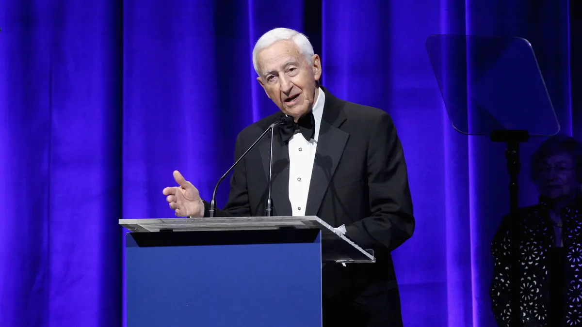 A man dressed in a suit speaks at an event.