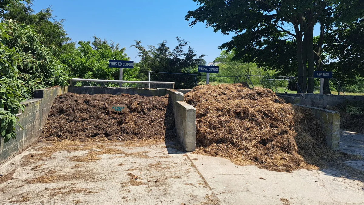 Two piles of brown material, labeled "Finished Compost" and "Almost Done!" are separated by cinderblocks on a concrete pad outside.