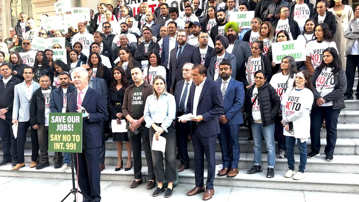 A speaker at a podium that reads "SAVE OUR JOBS!" in front of a crowd of people on steps.