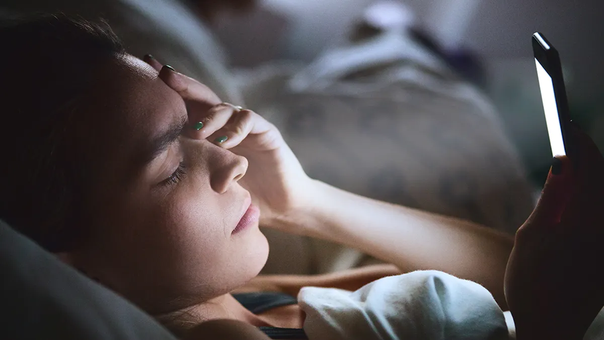 Woman in bed with phone, headache.