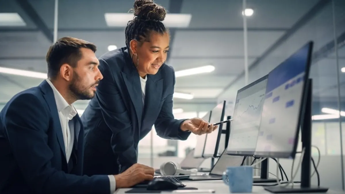 Two colleagues looking at a line chart on a monitor in an office.