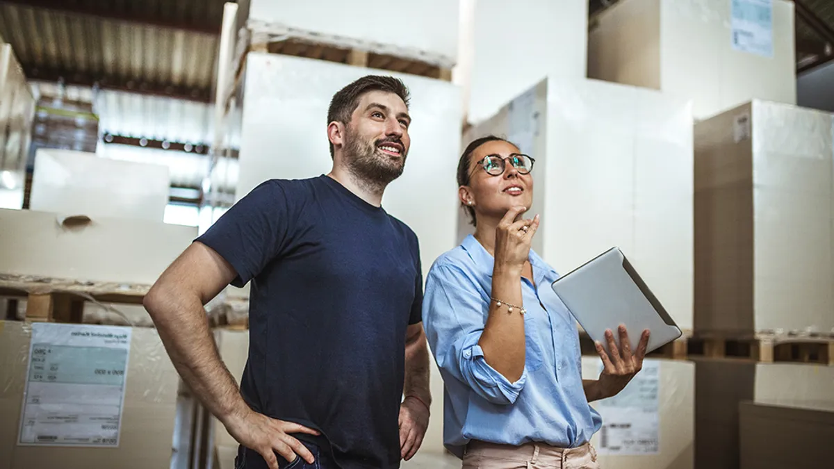 Two people, one of whom is holding a tablet, are doing a delivery check in a warehouse.