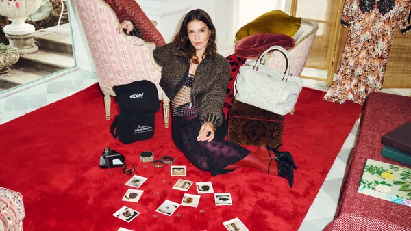 A person sits on a red carpeted floor and leans on a chair. A group of Polaroid pictures are scattered in front of her.