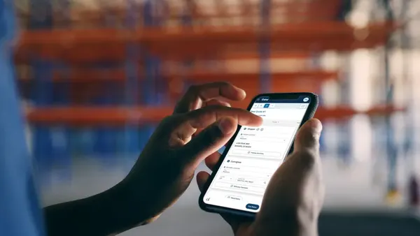 A person's hands hold and use a mobile platform on a phone to demonstrate how freight can be booked and monitored.