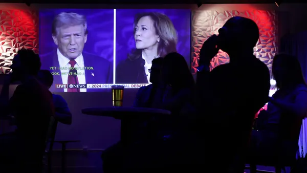 People in a bar watch a TV screen with former President Donald Trump and Vice President Kamala Harrris debating.