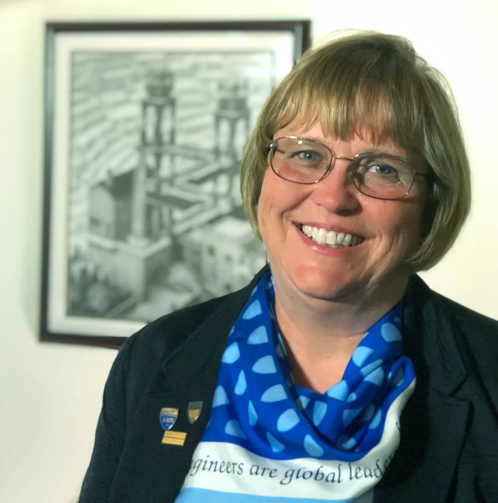 A smiling woman with a short blond bob haircut and glasses.