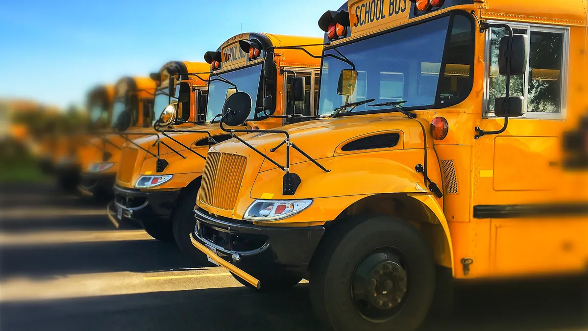 A row of yellow school buses are lined up on asphalt against a blue sky.