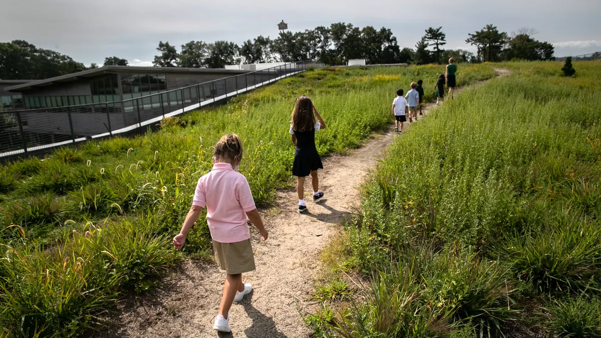 Young students walk on a path in a field near a school.