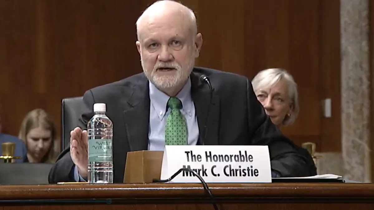 A man speaks at a table with a placard saying "Mark Christie."