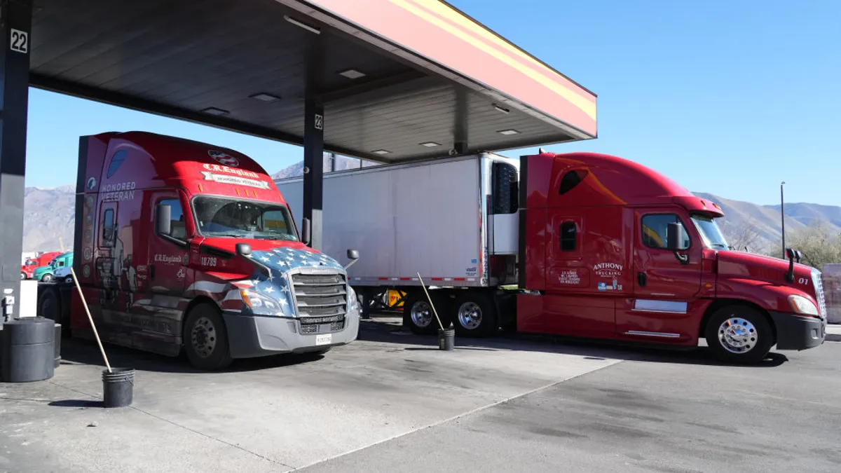 Two trucks at a fueling station with a mountain ridge in the background.