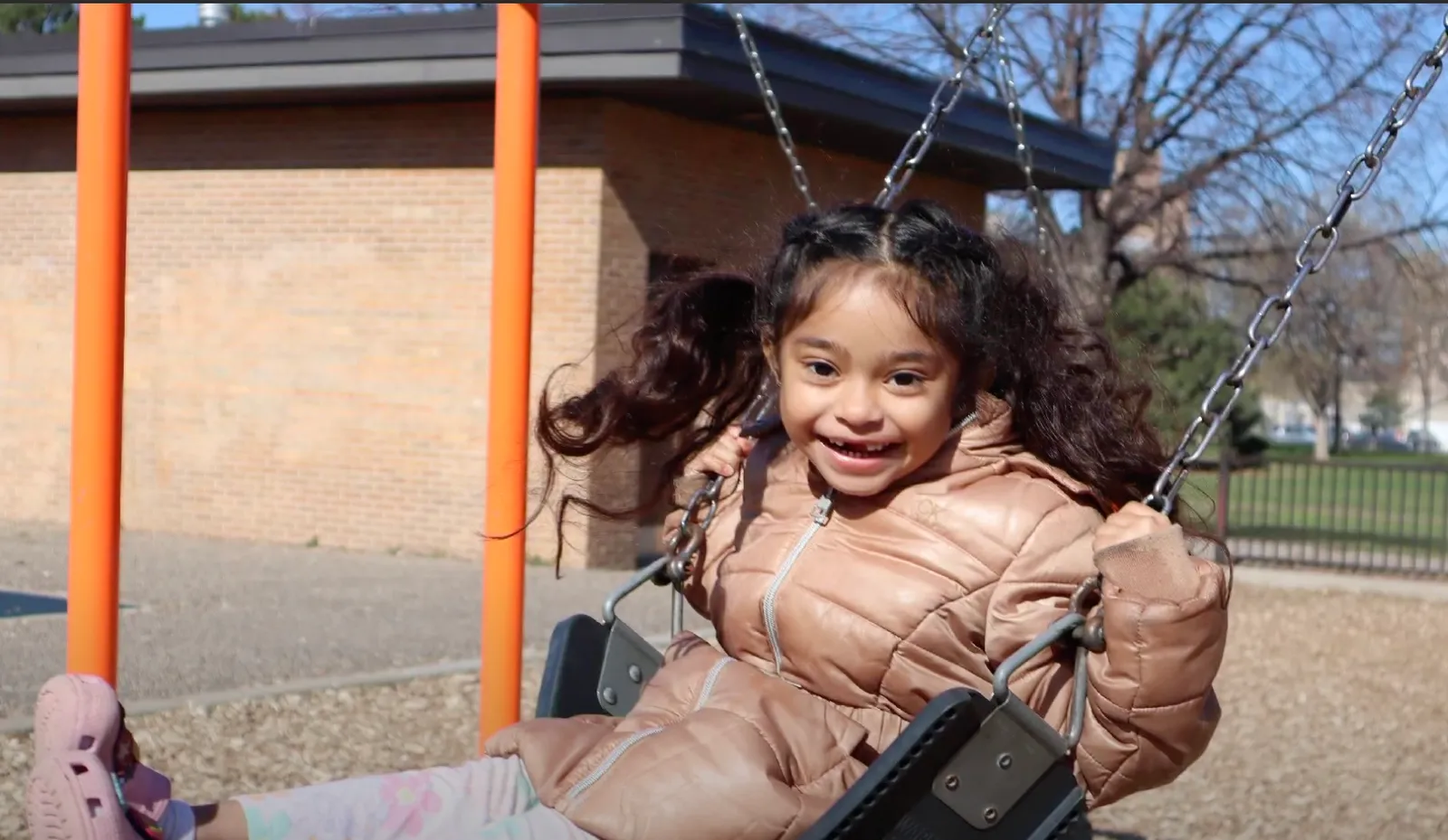 A young student is looking at the camera while on a swing outside a building.