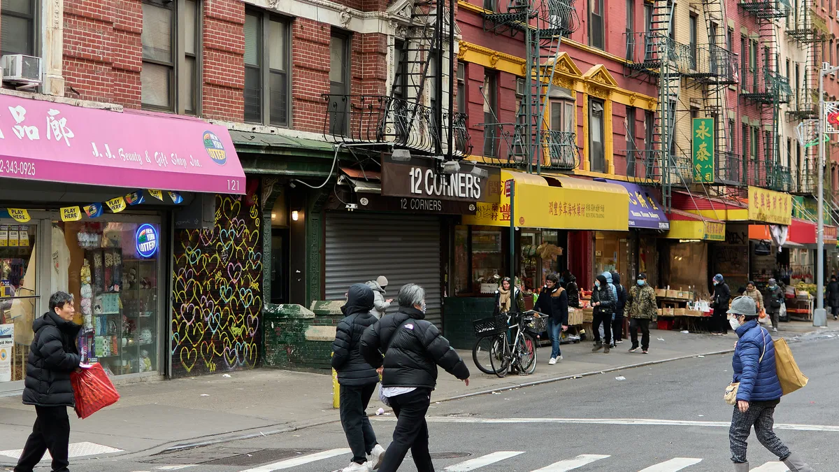 A city street lined with small storefronts. People walk across the street at a crosswalk.