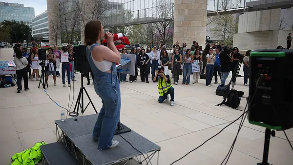 Students gather to protest outside the U.S. Department of Education headquarters. One student is in the center and has a megaphone.