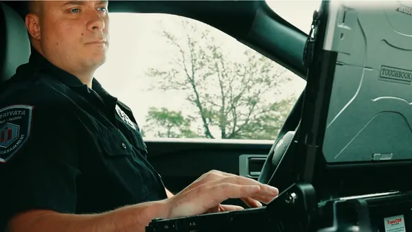 A police officer works on a laptop inside a patrol car.