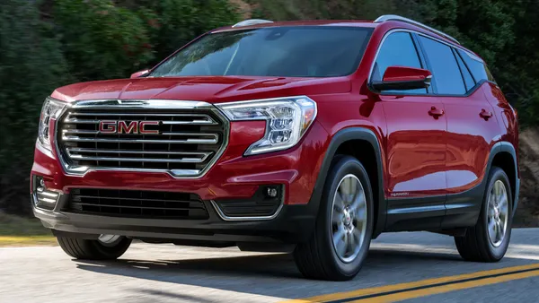 A red 2023 GMC Terrain SLT SUV driving on a road with greenery in the background.