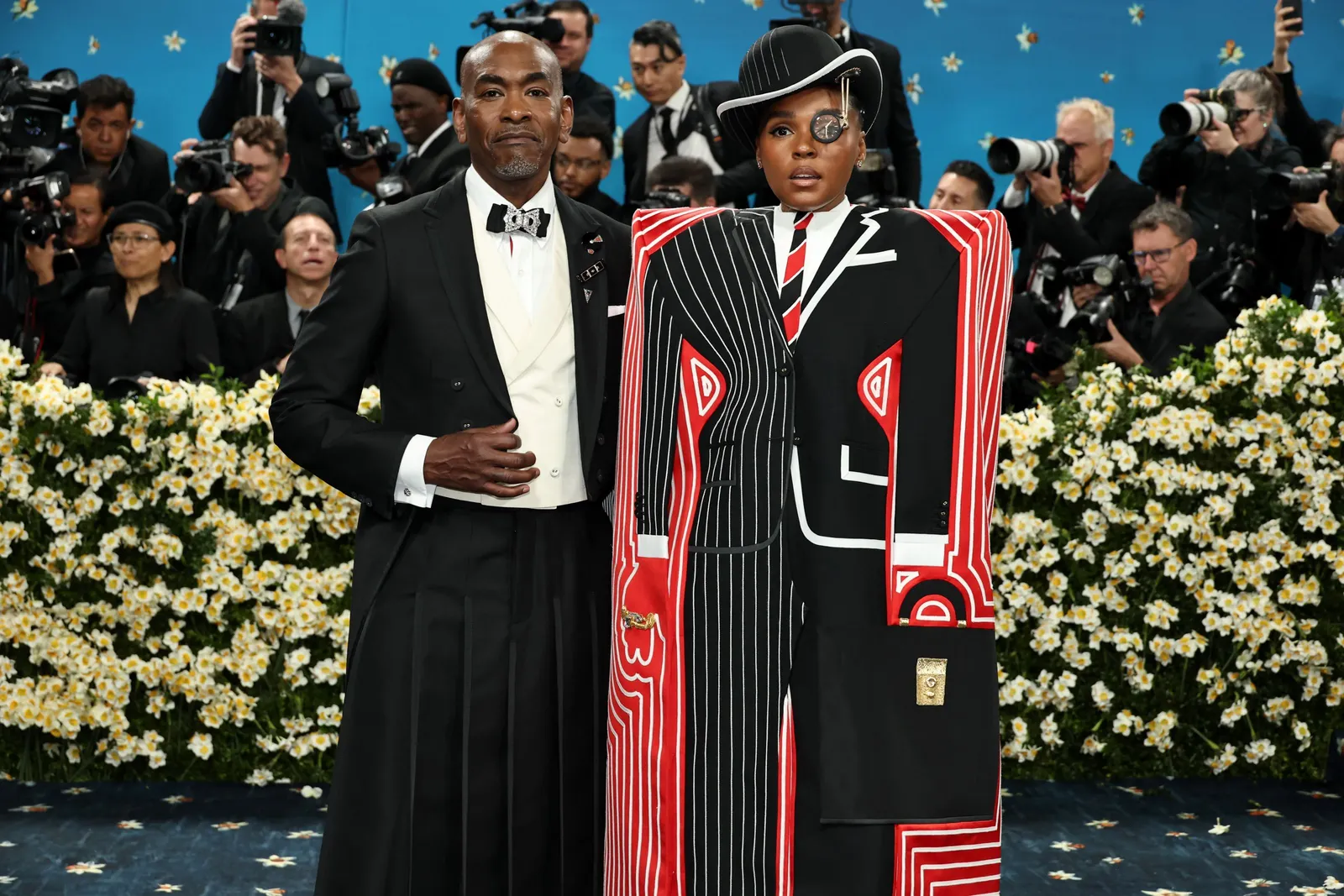 A man in a black skirted suit stands next to a person in an avant-garde skirted suit.