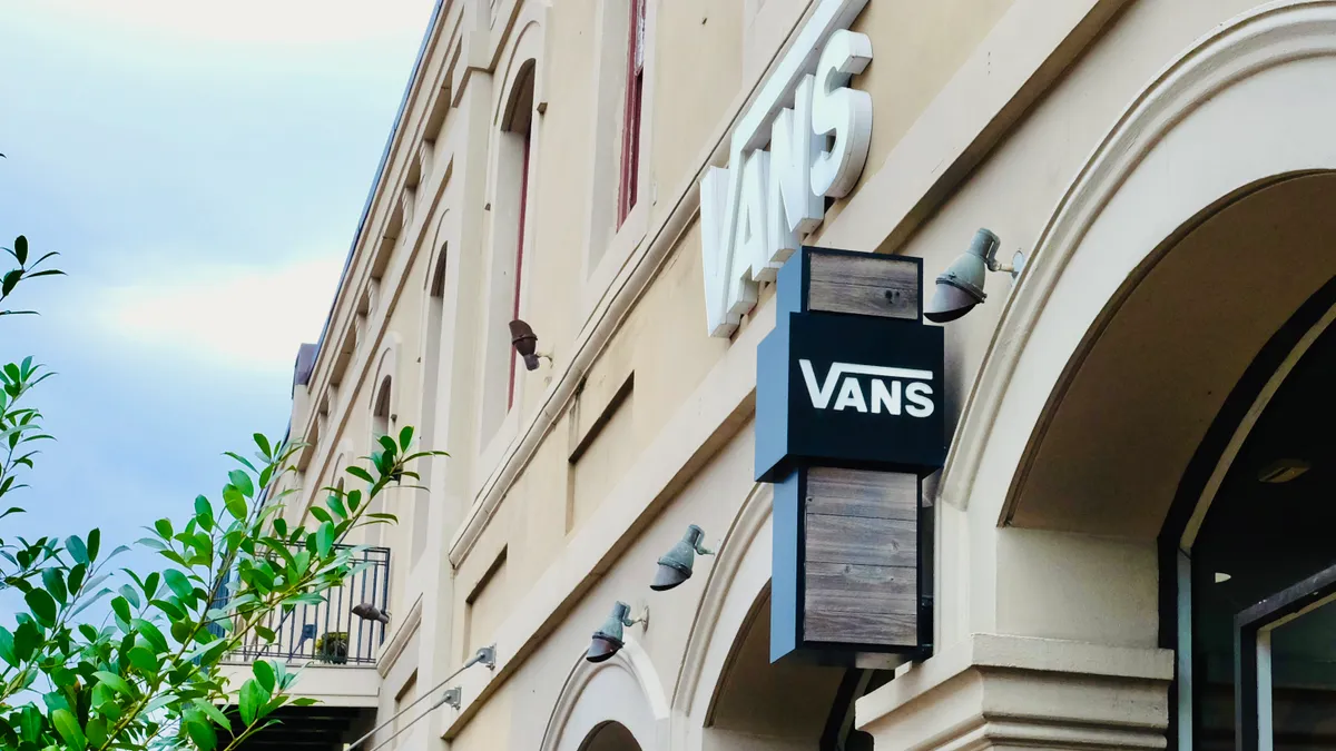 Signage reading "Vans" adorns a light-colored building with curved windows. A leafy tree branch peeks out from the left.