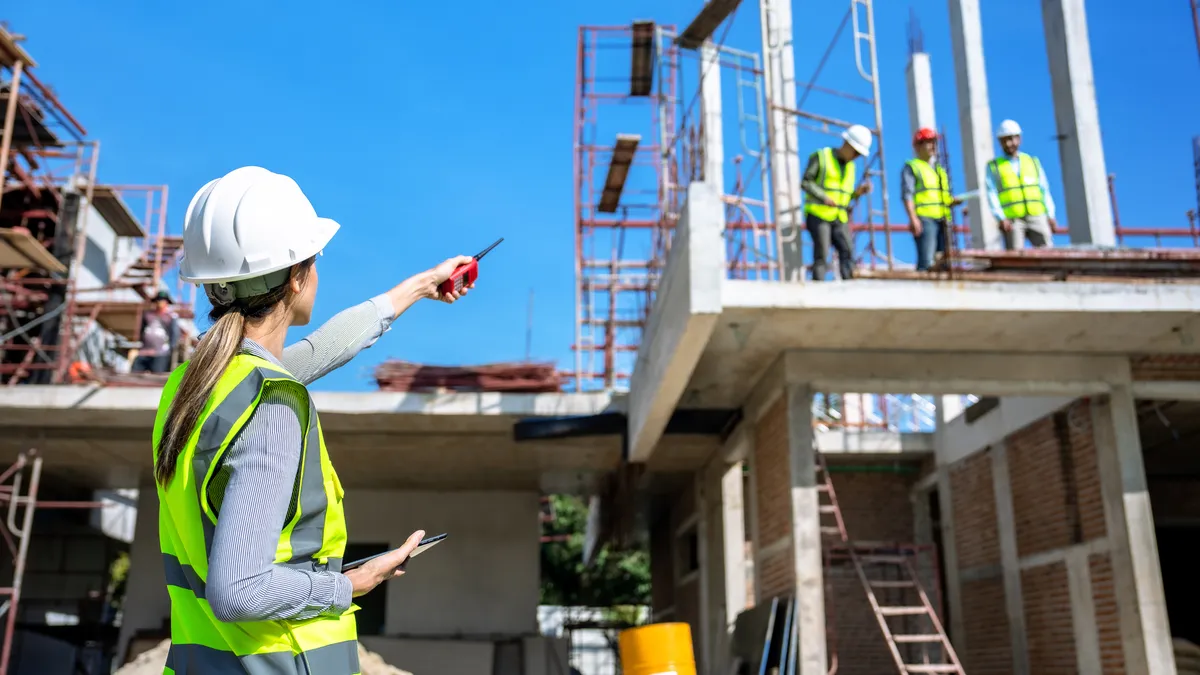 A construction worker communicates with more workers atop a structure being built.