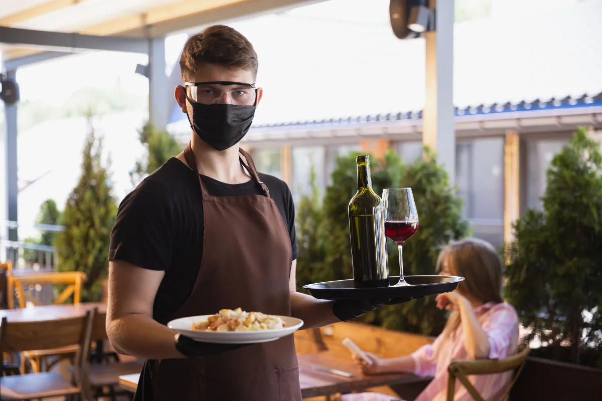 The waiter works in a restaurant in a medical mask, gloves during coronavirus pandemic.