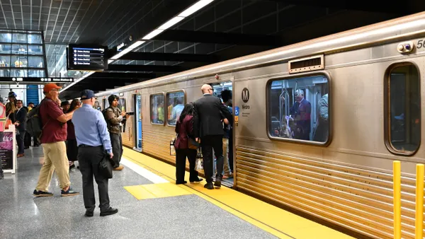 People stand on a subway platform next to a silver train.