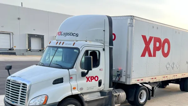 An XPO tractor-trailer parked at a facility in the sun.