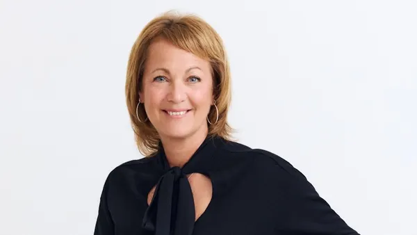 A person with hoop earrings and a black shirt with a bow is smiling.