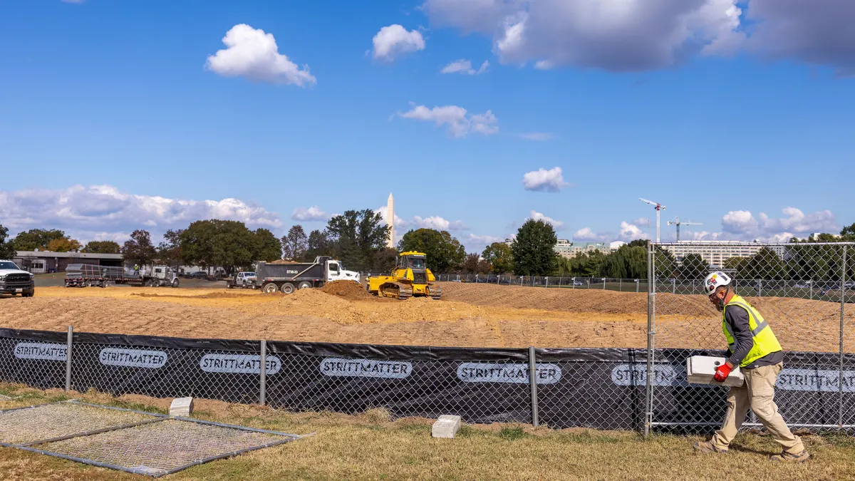 Workers build a fence as trucks unload debris and soil from the demolition of the White House's East Wing