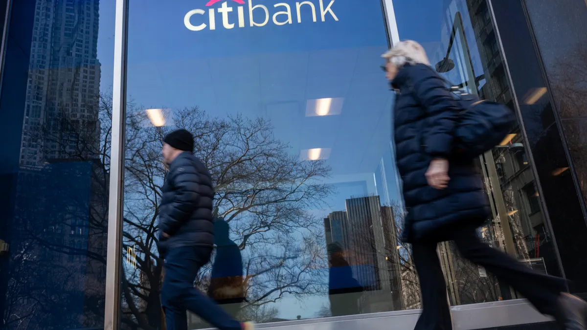 Two people walk by a Citi branch in a downtown setting