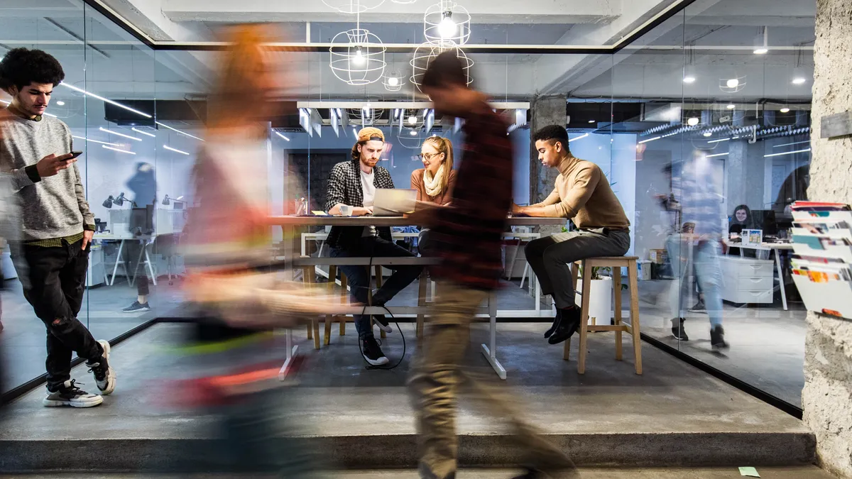 A group of individual work in a modern office while others walk by.