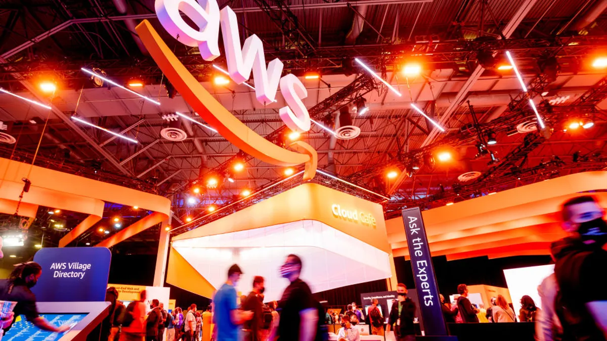 Bright AWS signage hangs over a trade show floor, attendees walking by in the foreground