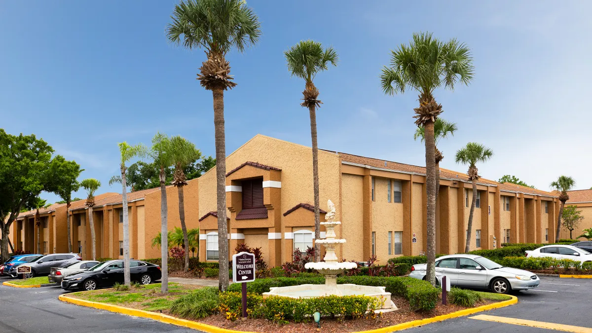 Brown, two-story apartments in Florida surrounded by palm trees and cares.