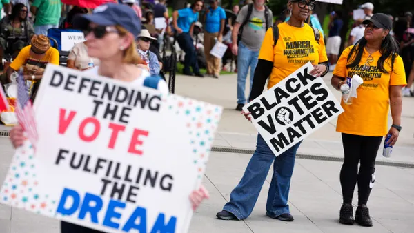 People at a protest holding signs that say "Defending the Vote, Fulfilling the Dream" and "Black Votes Matter"