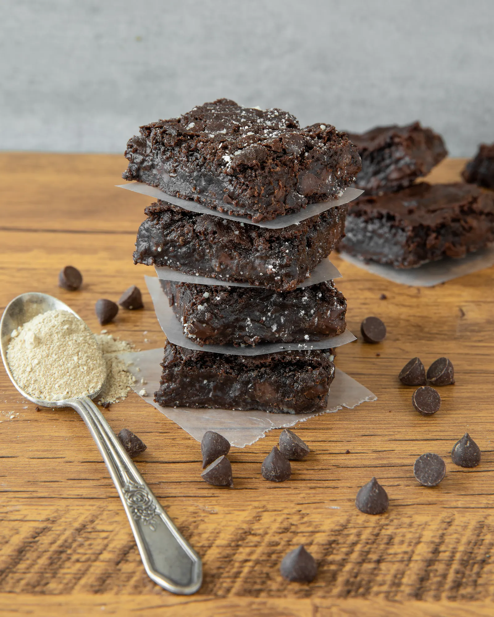 A stack of fudge brownies with a teaspoon filled with beige Rhiza protein to the left.