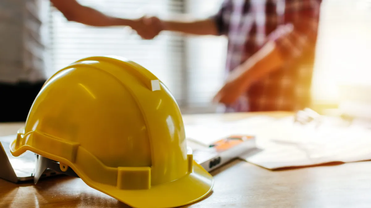 People shaking hands behind construction hat