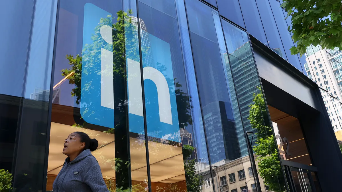 A pedestrian walks by a LinkedIn sign on an office building.