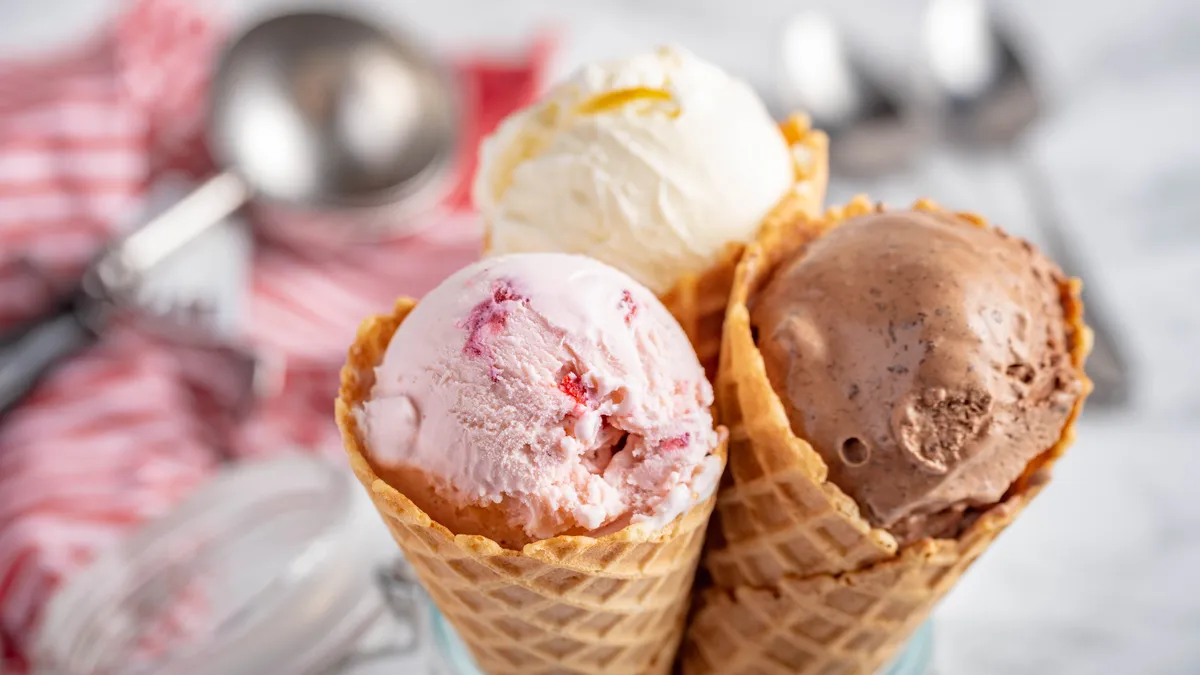 Cones of strawberry, vanilla and chocolate ice cream stick out of a glass jar with an ice cream scoop and spoons on a blurred counter background.