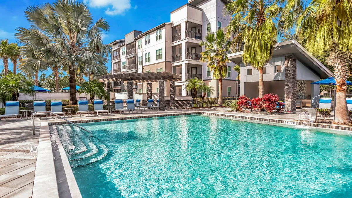 Pool in front of palm trees and a four-story new apartment building.