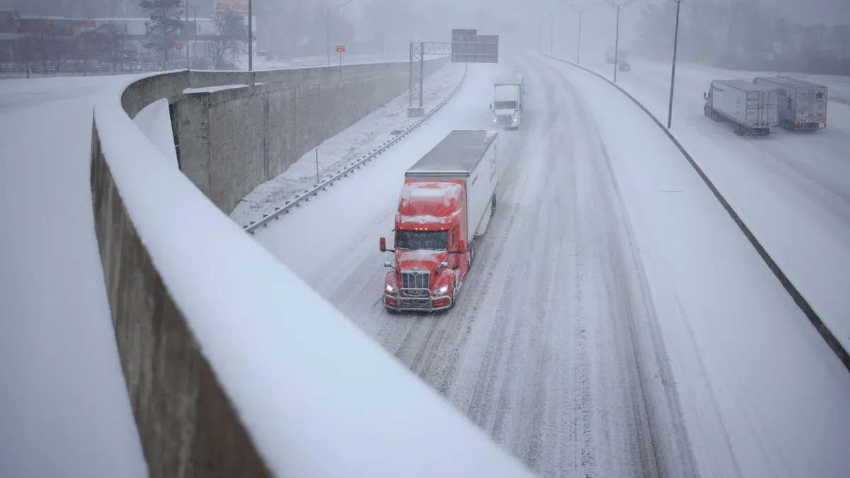 Trucks drive down a snowy highway.