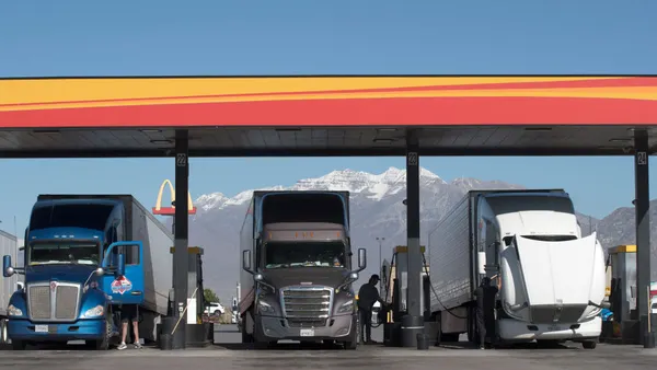 Truck drivers alongside their big rigs at a fuel station with a mountain range and McDonald's sign in the background.