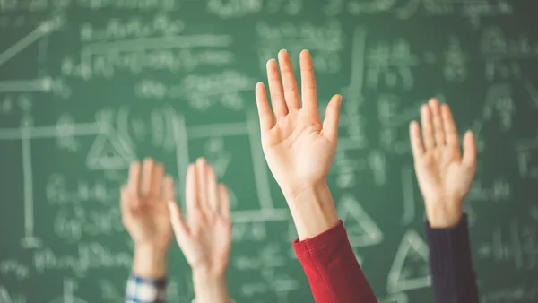 A couple of hands are raised. Behind the hands is a green chalkboard with math equations.