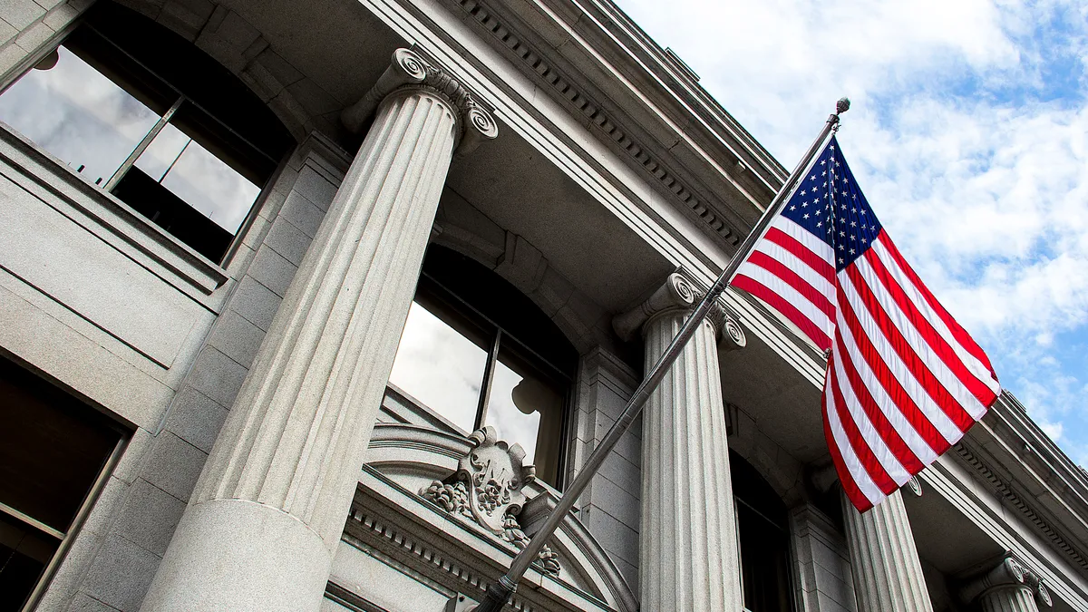 American flag flying over government building in city, blue sky and clouds