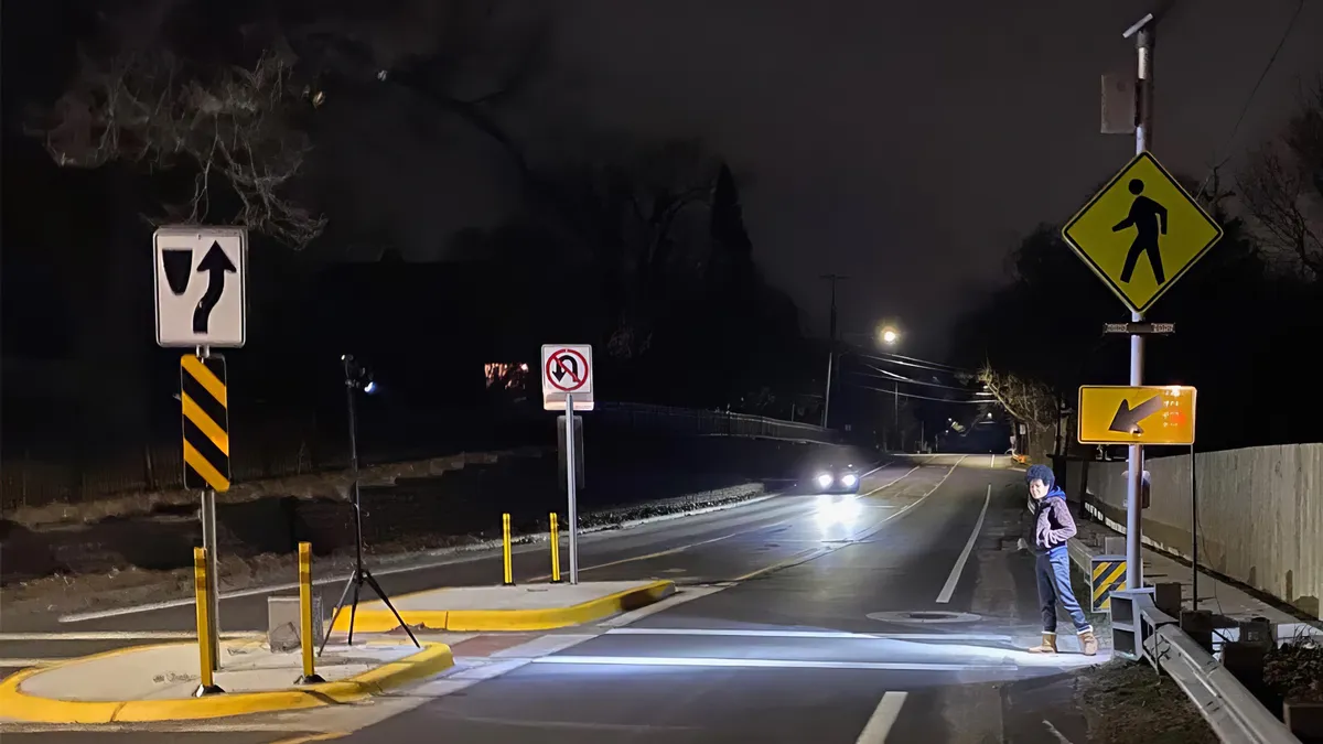 A light shines across a crosswalk at night as a pedestrian starts to cross.