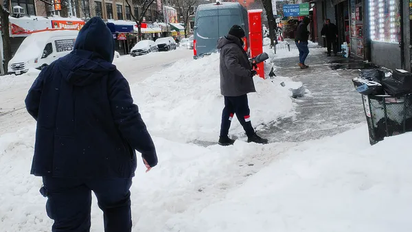 People shovel snow off a sidewalk.