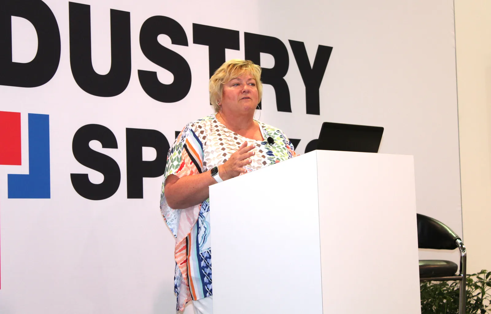 A person speaks at a conference from behind a white podium.