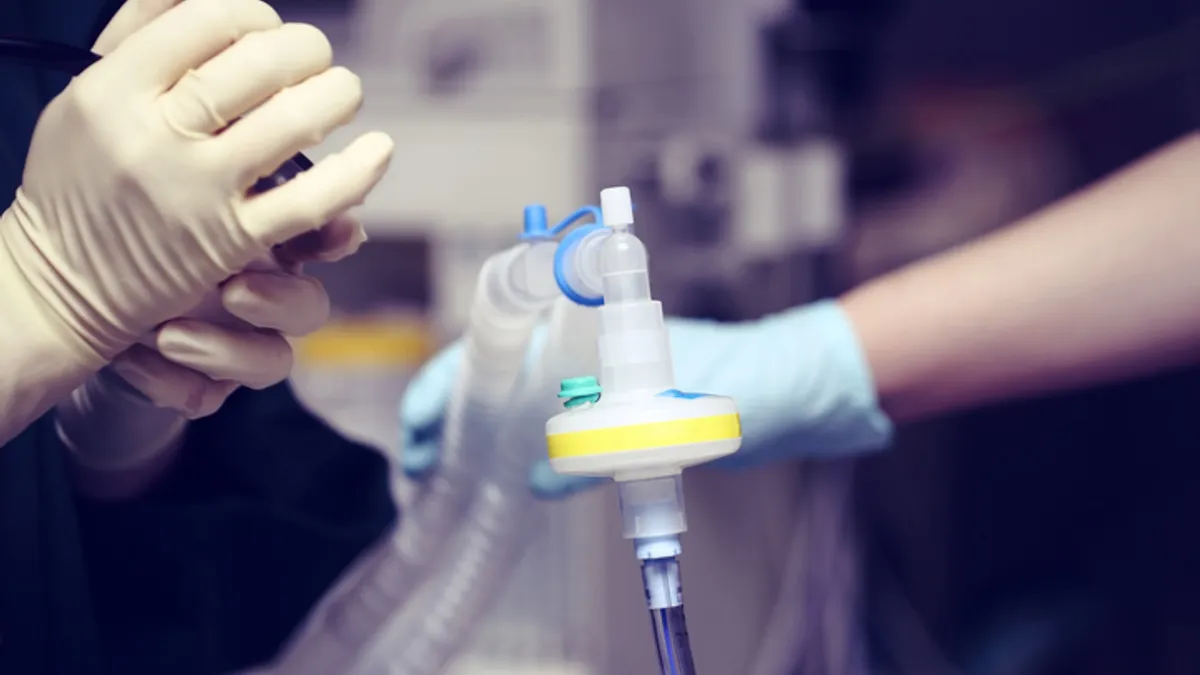 One person wears white gloves while another holds an airway tube